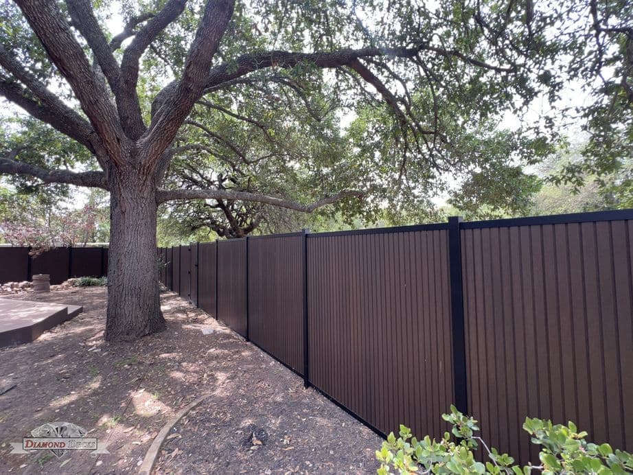 Brown composite privacy fence beneath mature oak trees, San Antonio, TX