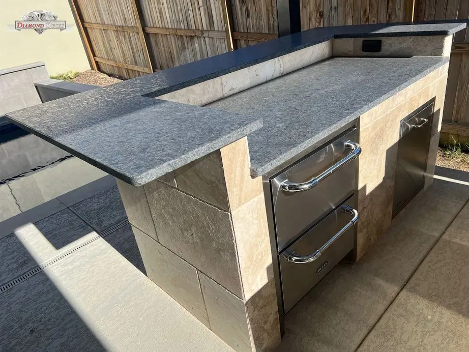 Travertine island with gray granite raised bar beside pool by Diamond Decks in San Antonio, TX