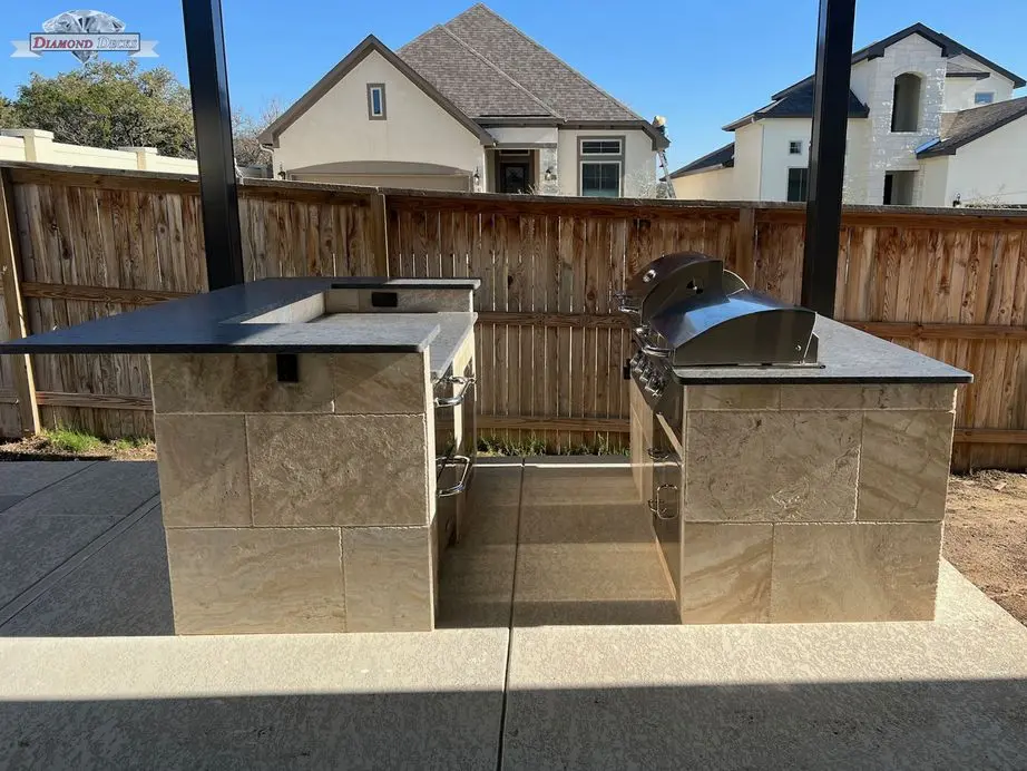 Two-piece travertine kitchen with black granite and grill by Diamond Decks in San Antonio, TX