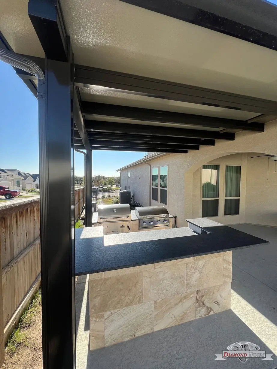 Black steel patio cover over travertine kitchen island by Diamond Decks in San Antonio, TX