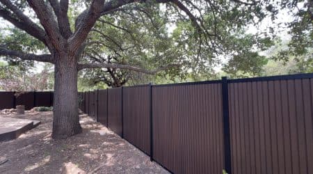 Brown composite privacy fence beneath mature oak trees, San Antonio, TX