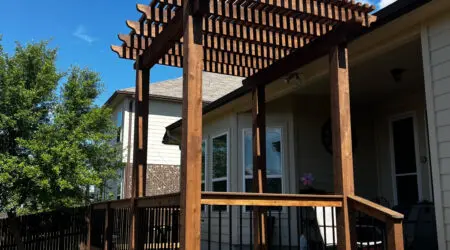 Dark-stained cedar pergola over composite deck with black baluster railing by Diamond Decks, San Antonio TX