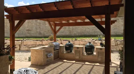Cedar pergola with slatted roof over limestone kitchen and smokers by Diamond Decks, San Antonio TX