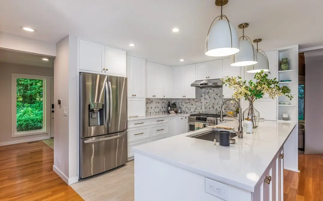 White shaker kitchen with triangle mosaic backsplash, brass knobs and white dome pendants over the peninsula