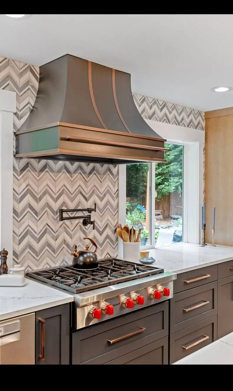 Custom black and copper range hood over a Wolf rangetop with chevron marble backsplash