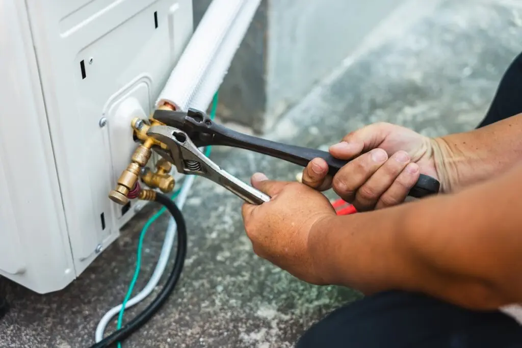 Air conditioner technician hands using wrenches to tighten flare nut on outdoor unit during installation, 