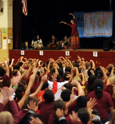Schoolkids raising their hands with Indian artists onstage.