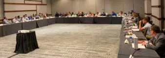 People gather at a horseshoe table in a hotel conference room.