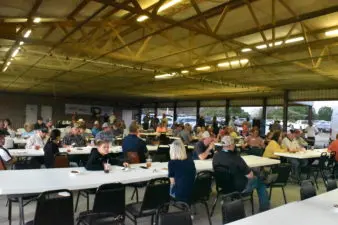 People sit and eat at several tables in a pavilion.