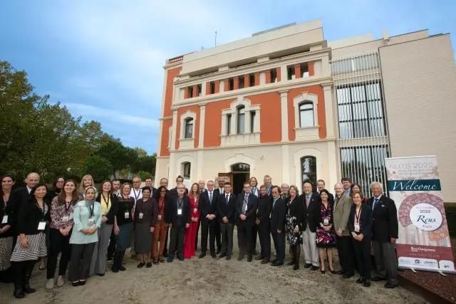 A group of people stand together for a photo outside next to a banner for the NUTS 2022 meeting.