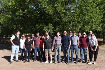 A group of people stand in front of mature pecan trees at an orchard in West Texas.