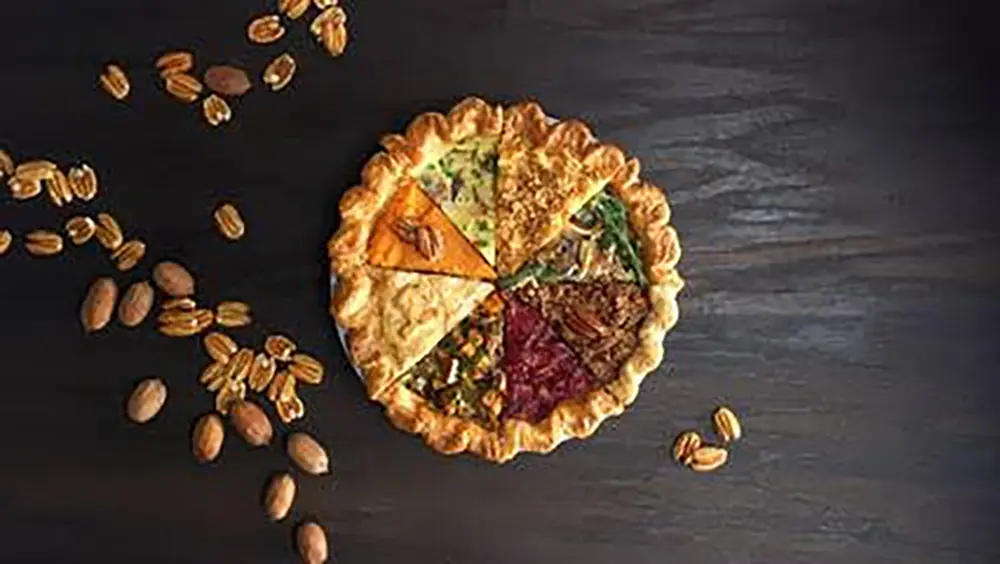 The ThanksEverything Pie sits on a table with some pecan halves scattered around it.