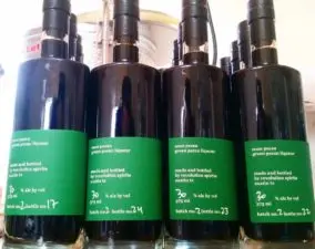 filled with Noce Pecan's Green Pecan Liqueur, glass bottles with a green labels sit on a shelf ready to be sold.