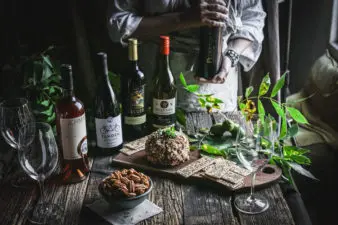 Four bottles of wine with accompanying glasses sit on display with a bowl of raw pecans and a pecan-crusted cheese ball. This picture demonstrates what can be found in the Texas Pecan and Wine tasting kit from the Texas Pecan Board.