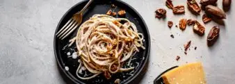 A dish of Linguine with Cauliflower Pecan Alfredo sits on a table next to cracked pecans and a block of cheese. APC plans to use plant-based recipes like this during Thanksgiving and the end of the year to market pecans.