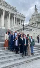 A group of people in business wear standing in front of the Capitol.