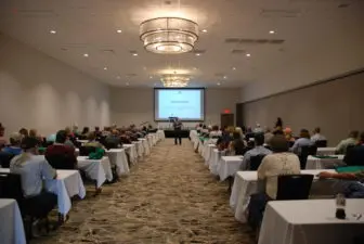 A man presents to a crowd of seated people at a conference.