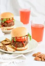 Fully dressed, Black Bean Pecan Burgers sit on plates with homemade fries next to glasses of juice.