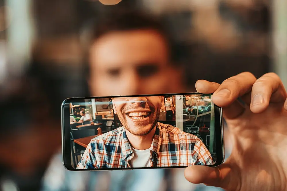 Man showing his new smile on his phone as a result of digital smile design in Brownsville, TX