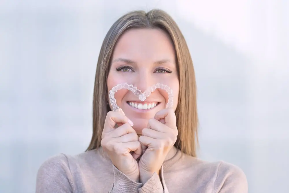 Woman smiling and holding invisalign aligners in the form of a heart