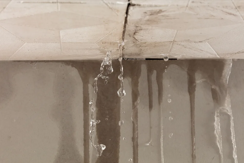 Rainwater leaking through a stained ceiling and running down an interior wall after a storm