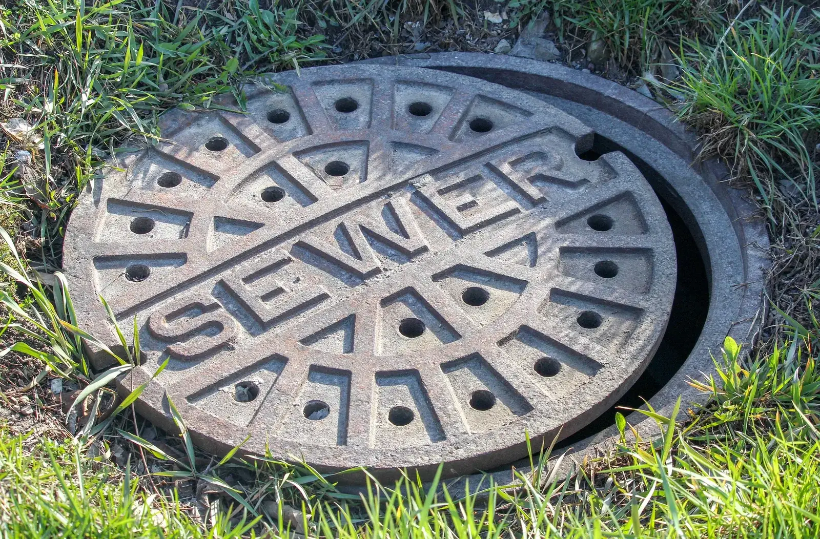 Cast iron sewer manhole cover set in a grassy lawn