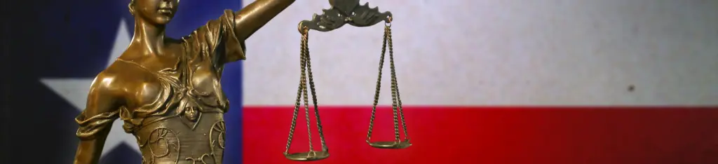Close-up of a small bronze statuette of Lady Justice before a flag of Texas.