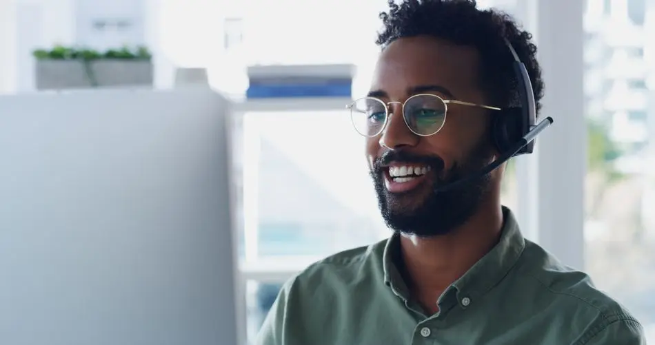 He's always ready to help Shot of a handsome young businessman wearing headsets while working on a computer in his office