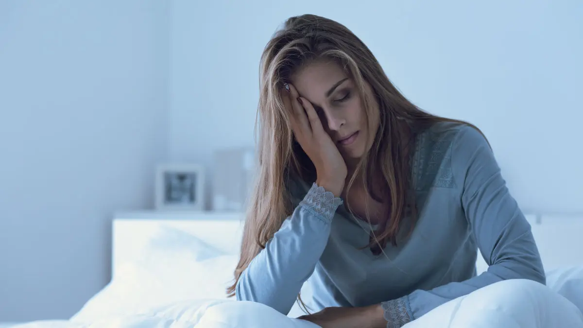 Tired woman sitting in bed with head in hand, suggesting sleep apnea symptoms