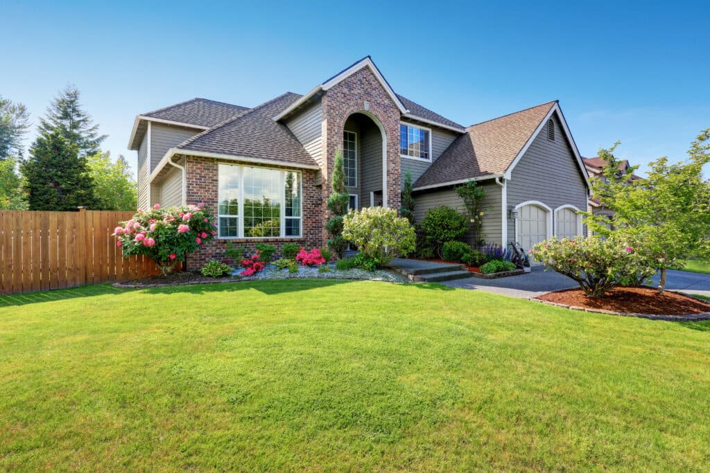 Luxury house exterior with brick and siding trim and double garage. Well kept garden around.