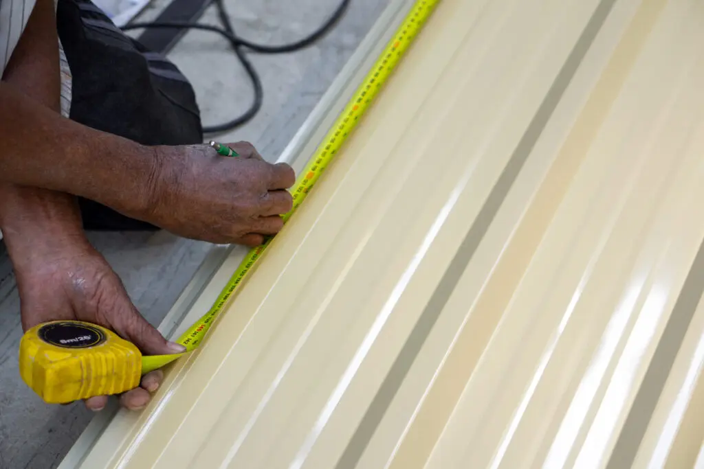 how to measure a roof for metal roofing A person is using a yellow measuring tape to measure sheet metal in a workshop. The focus is on precise measurement for future task.
