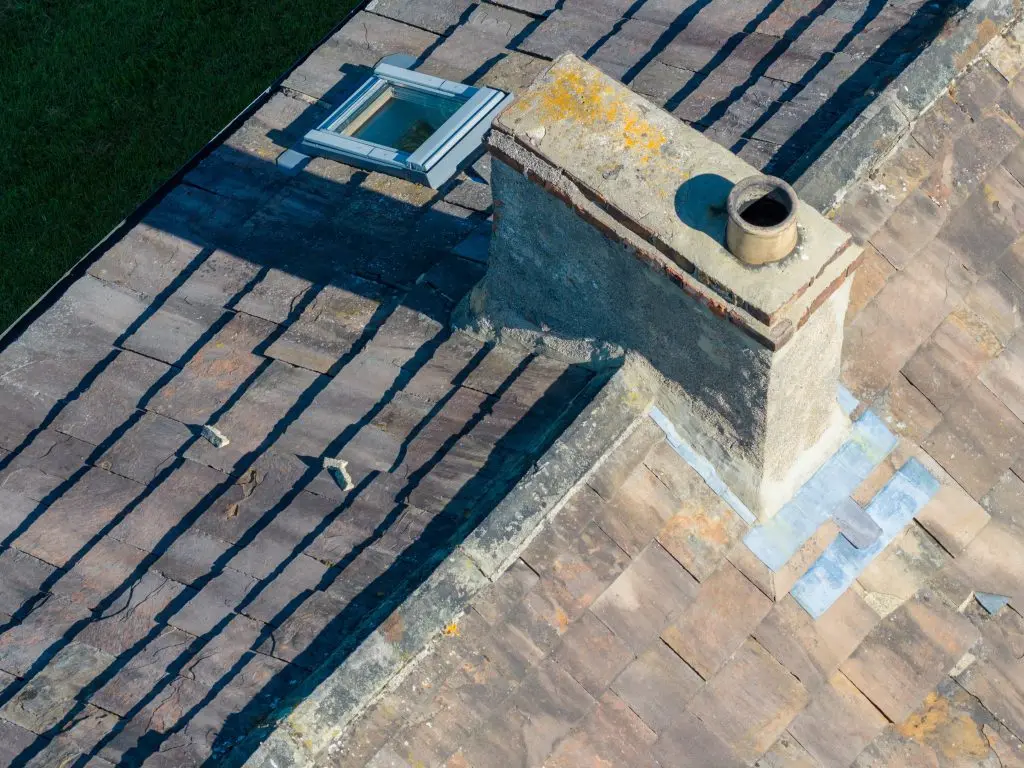 chimney flashing repair Aerial view of traditional slate roof with chimney stack roof window and repaired lead flashing showing ageing roofing materials cracked slates and residential property maintenance issues from above