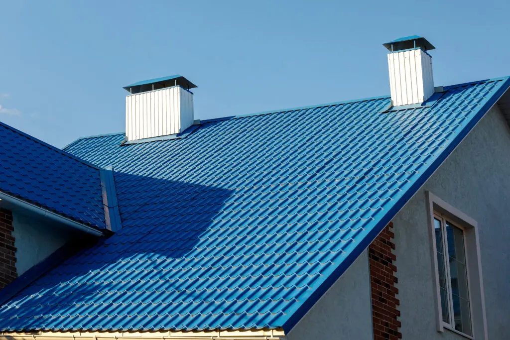 metal roof colors A roof of a house or cottage made of blue metal tiles with drains, slopes and chimney against the blue sky. Copy space