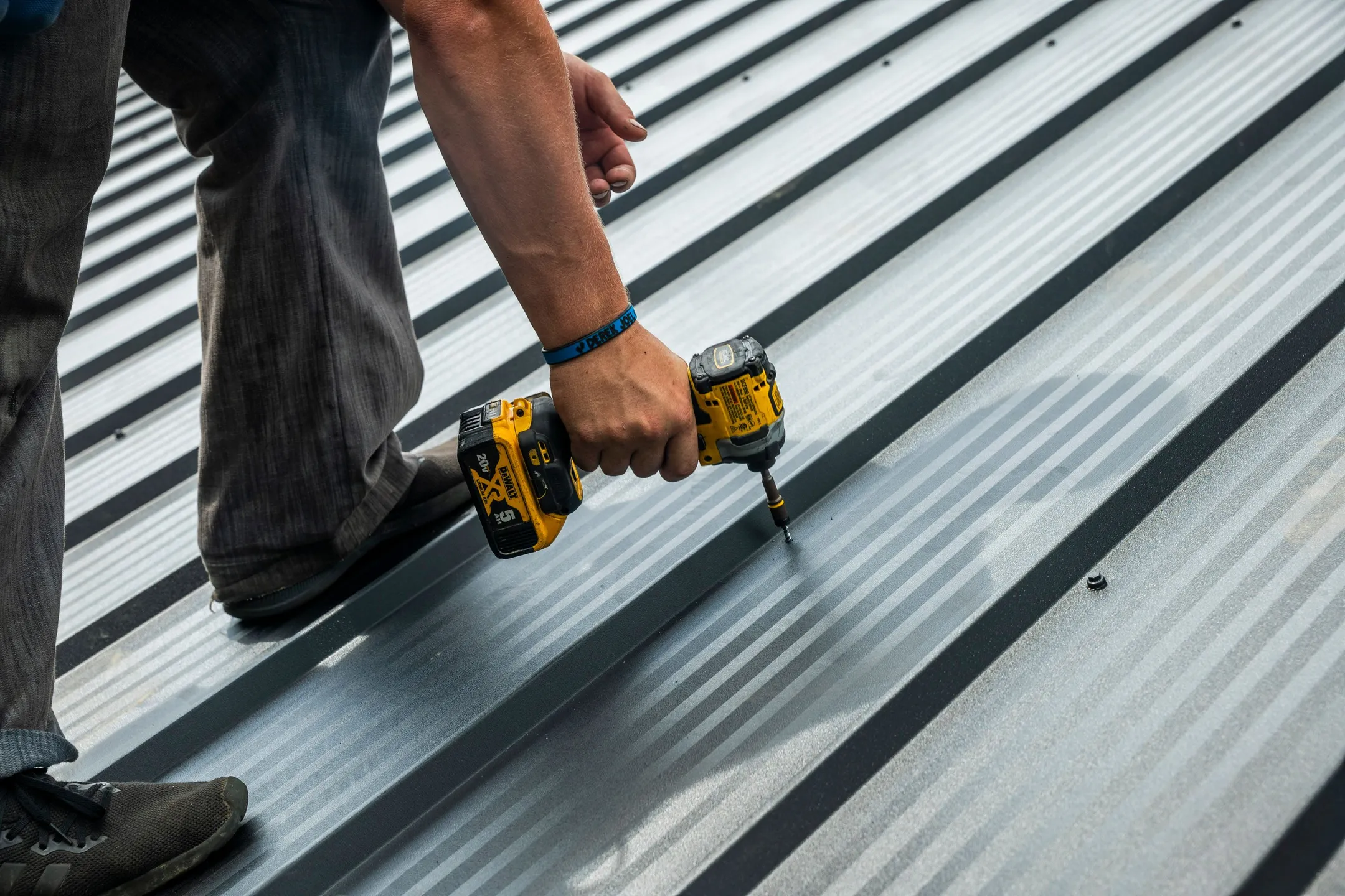 person screwing gray metal roof panel