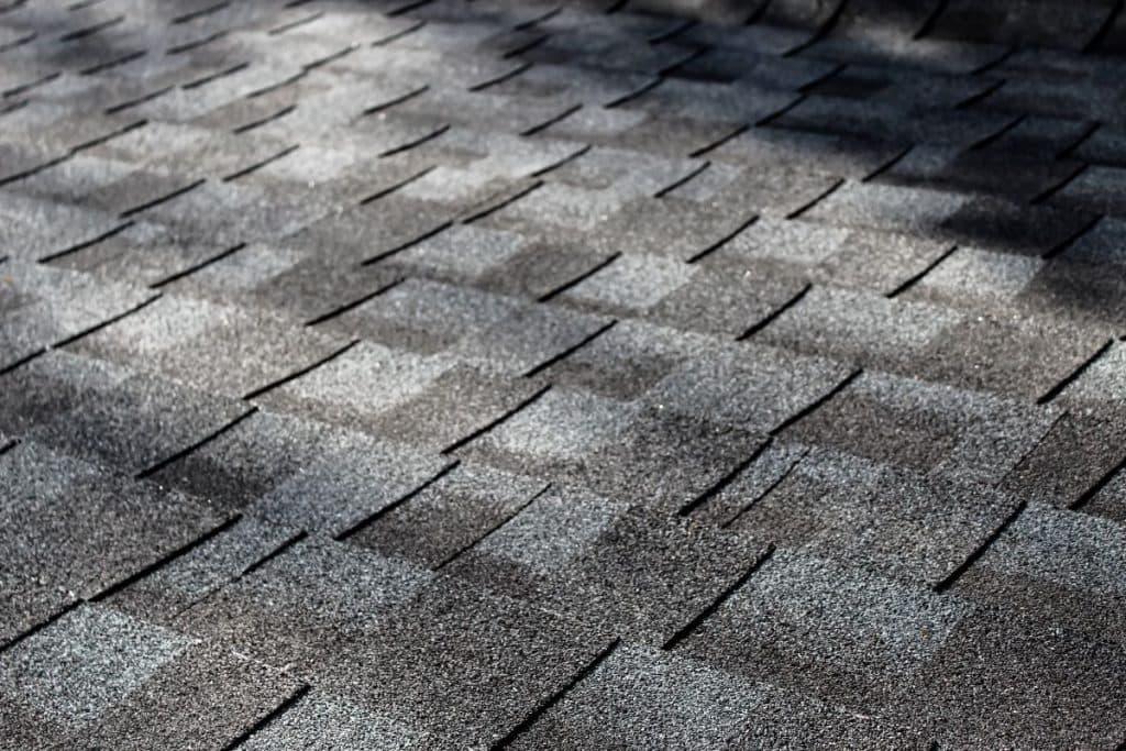 close-up of an asphalt shingle roof at an angle with dappled sunlight
