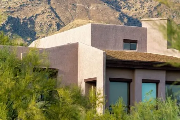 Stucco contractor in New Mexico recent project: Adobe style house with flat roof and block features with visible windows and chimneys in the late afternoon sun and shade