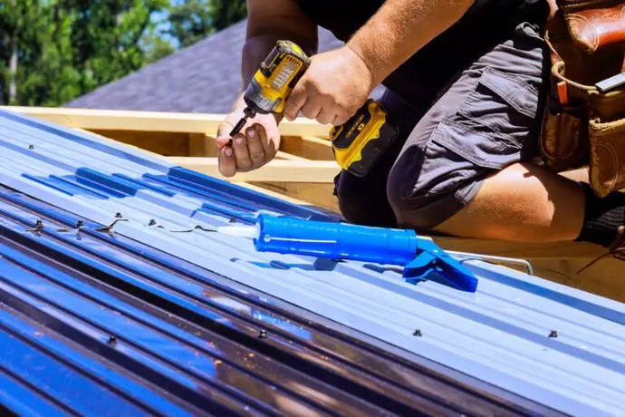 metal roof maintenance checklist Worker uses drill, sealant while installing metal roof at house.