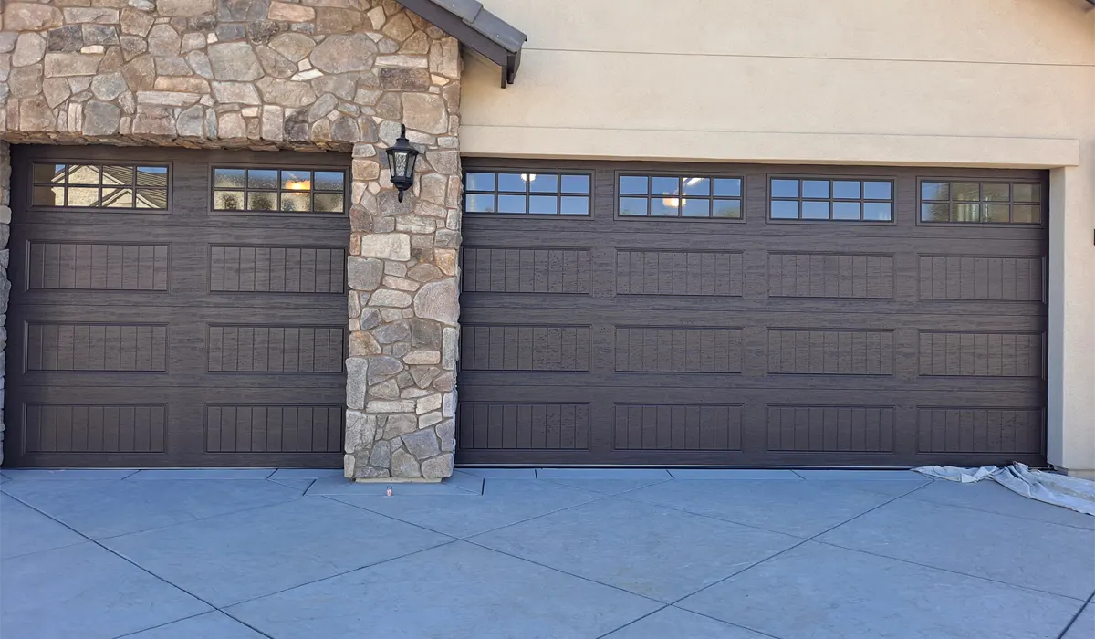 Two dark brown carriage-style garage doors with window tops beside a stone pillar