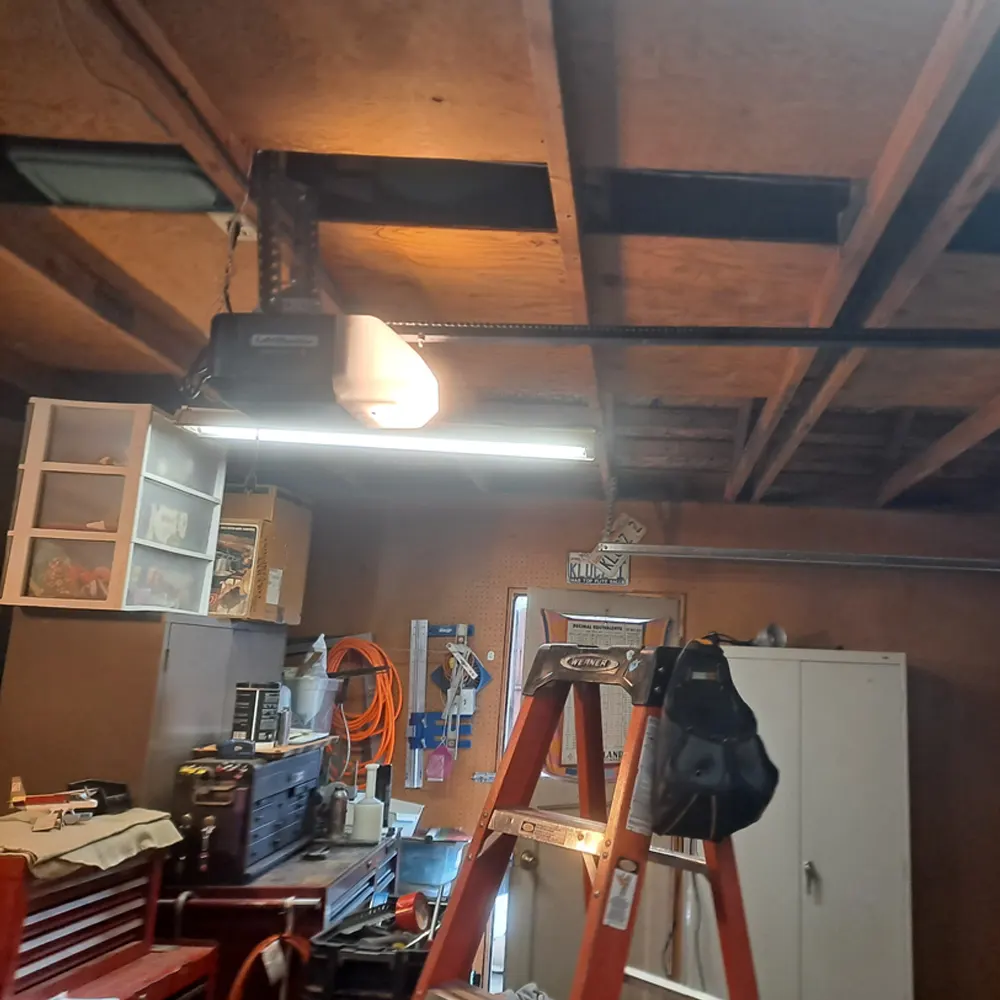 Garage door opener mounted on the ceiling of a workshop garage, with a ladder set up beneath it