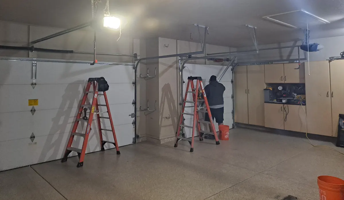 Technician on a ladder working on a garage door in a finished garage
