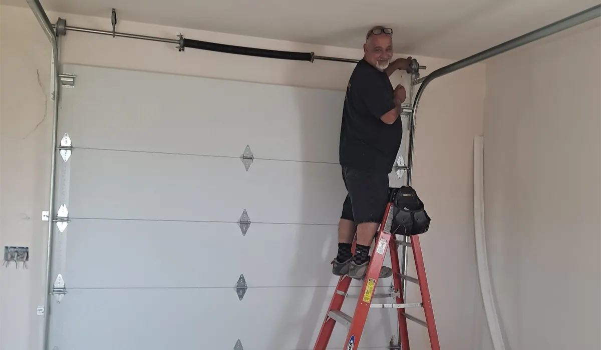 Technician on a ladder adjusting a garage door's spring and track