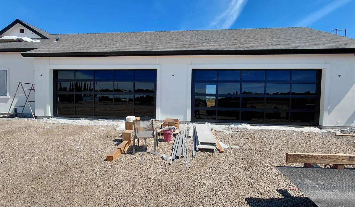 Two new full-view glass garage doors on a new home, with installation materials on the driveway