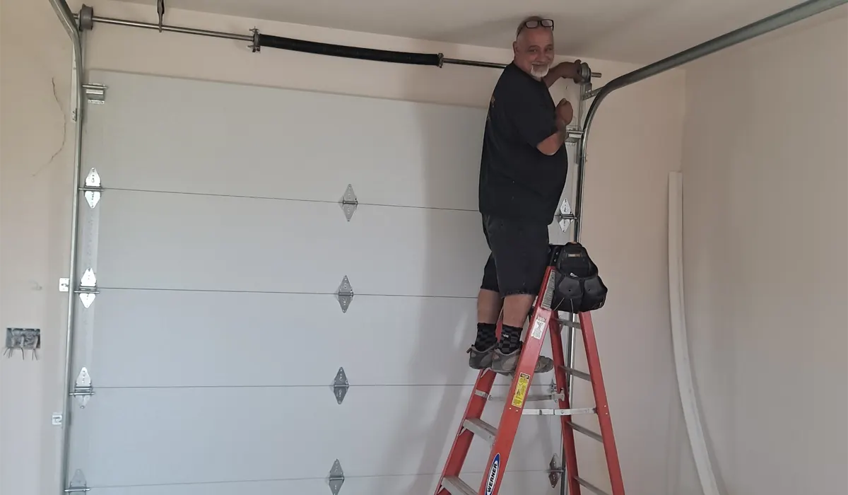Technician on a ladder working on the track and spring of a new white garage door