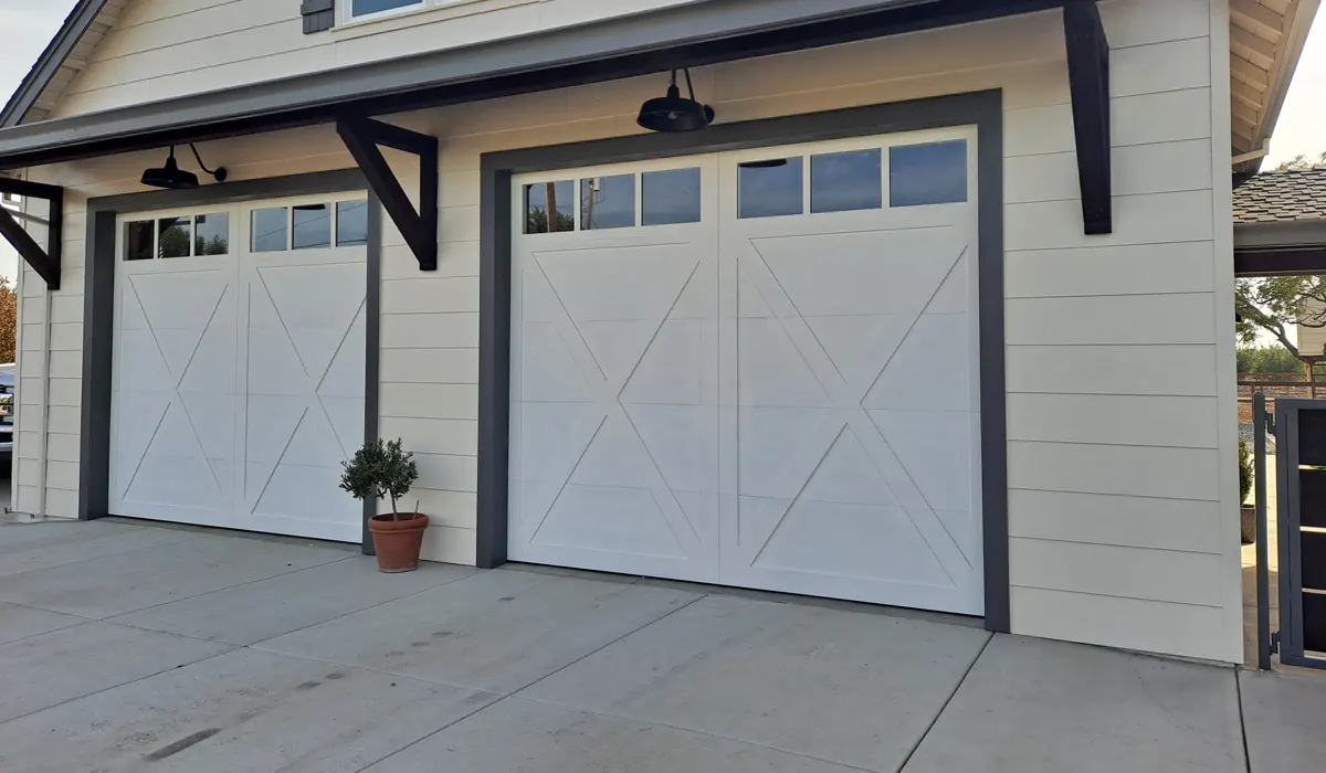 Two white carriage-style garage doors with X-brace panels and window tops on a craftsman-style home