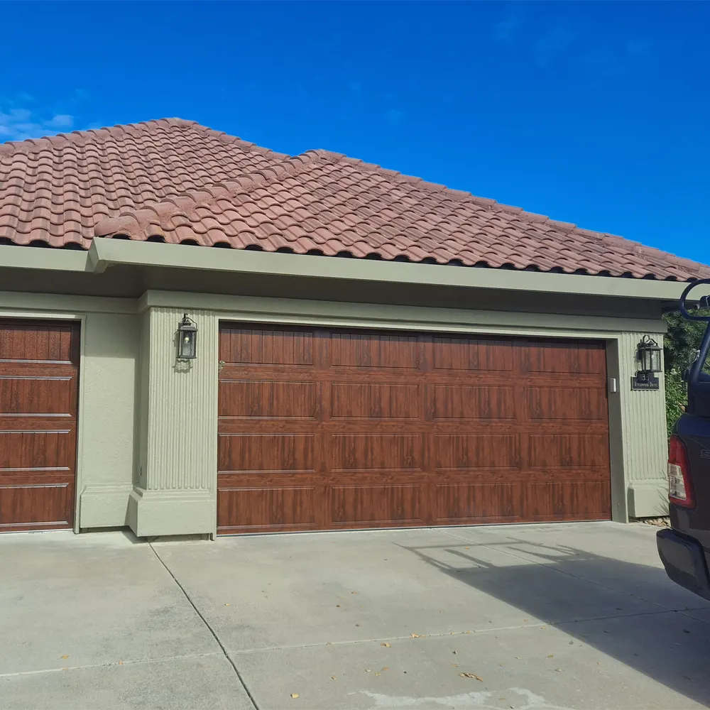 Two wood-grain carriage-style garage doors on a home with a red tile roof