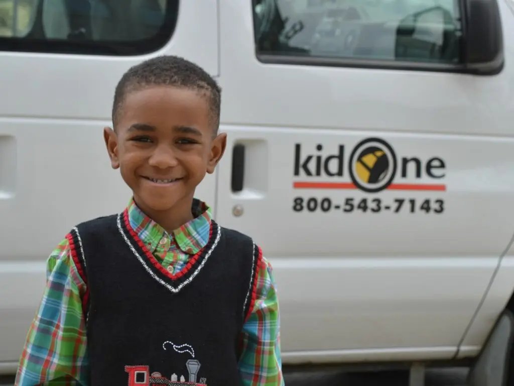 Boy smiles as he poses in front of a Kid One van