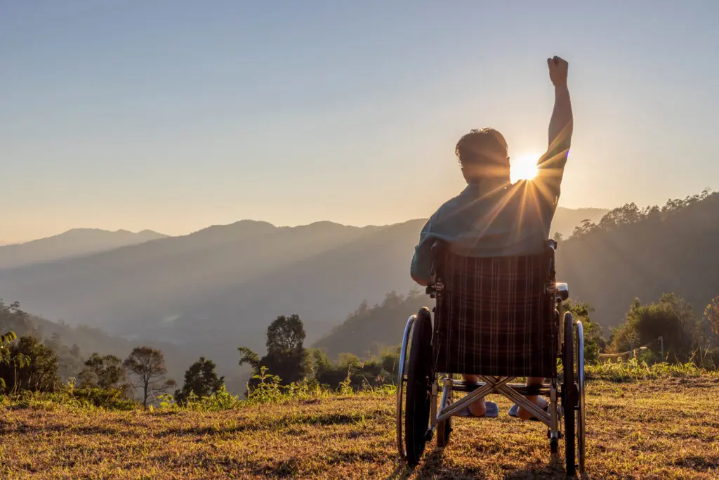 Silhouette of happy disabled man in a wheelchair and stretching hands at sunset. back view,