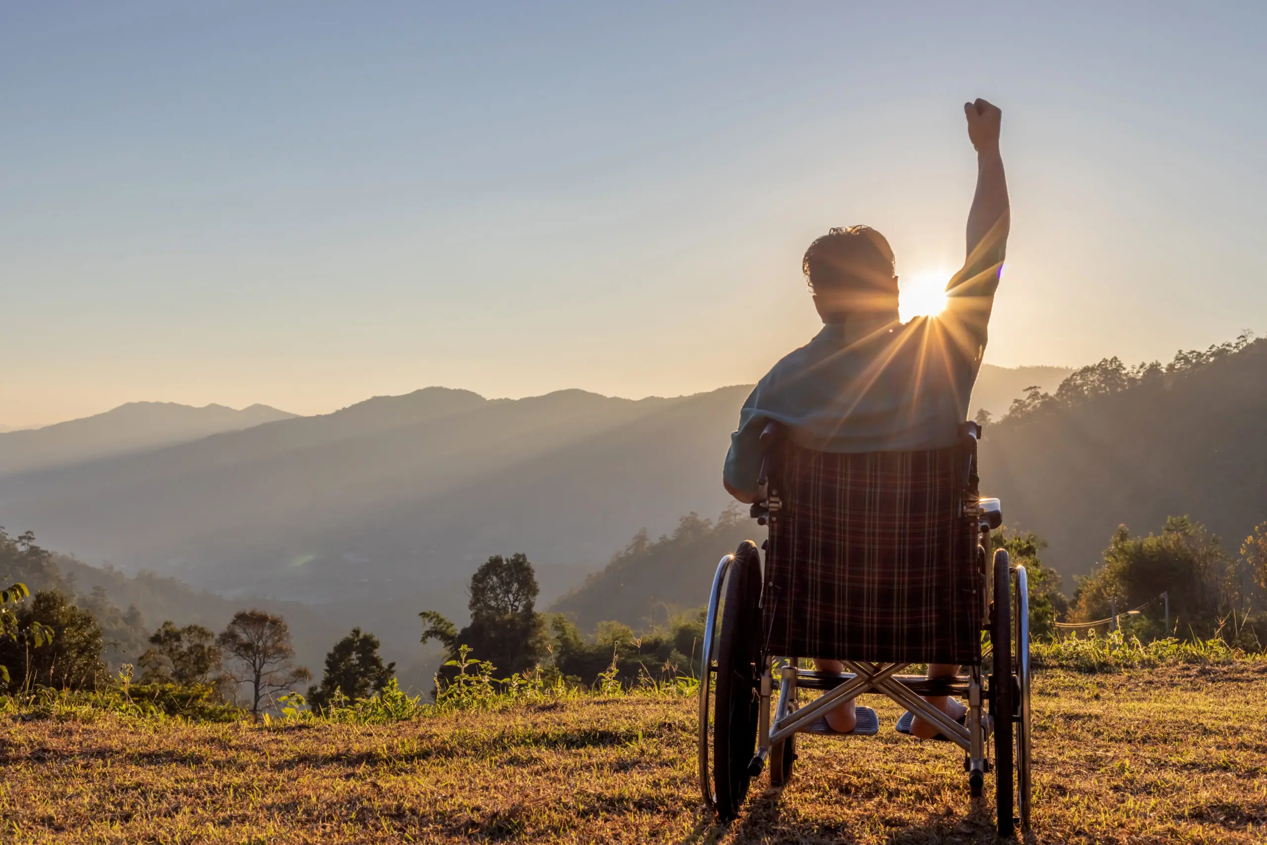 Silhouette of happy disabled man in a wheelchair and stretching hands at sunset. back view,