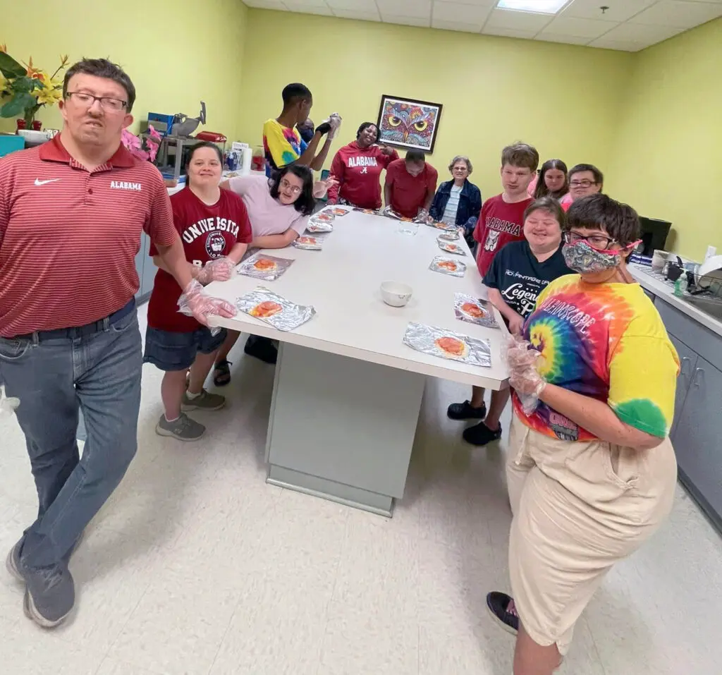 A group of younger adults stand around a table filled with pizza ingredients