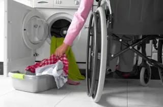 Person in a wheelchair putting laundry in a dryer